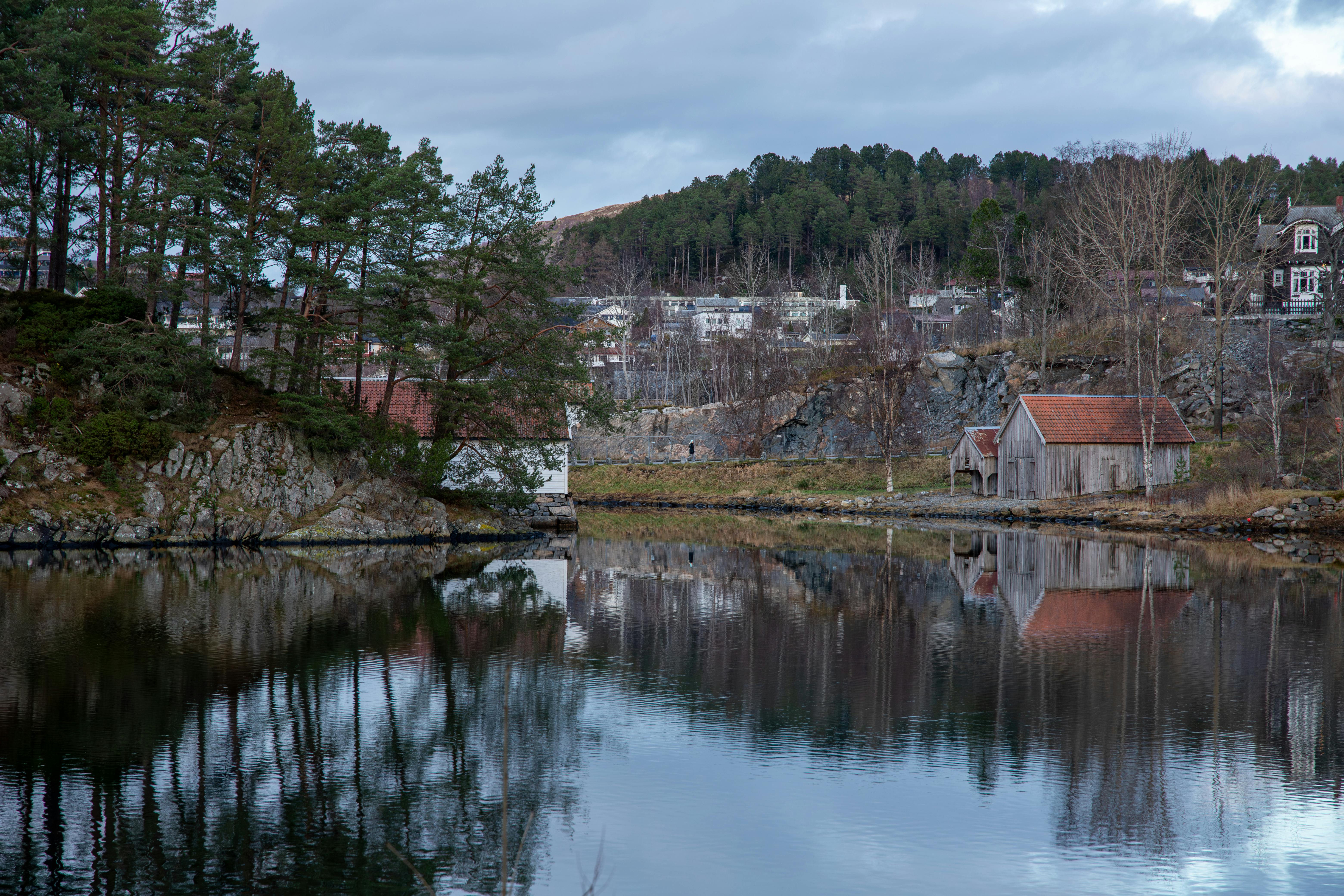 Tranquil lakeside scene in Ålesund, Norway, with rustic boathouses and serene reflections.