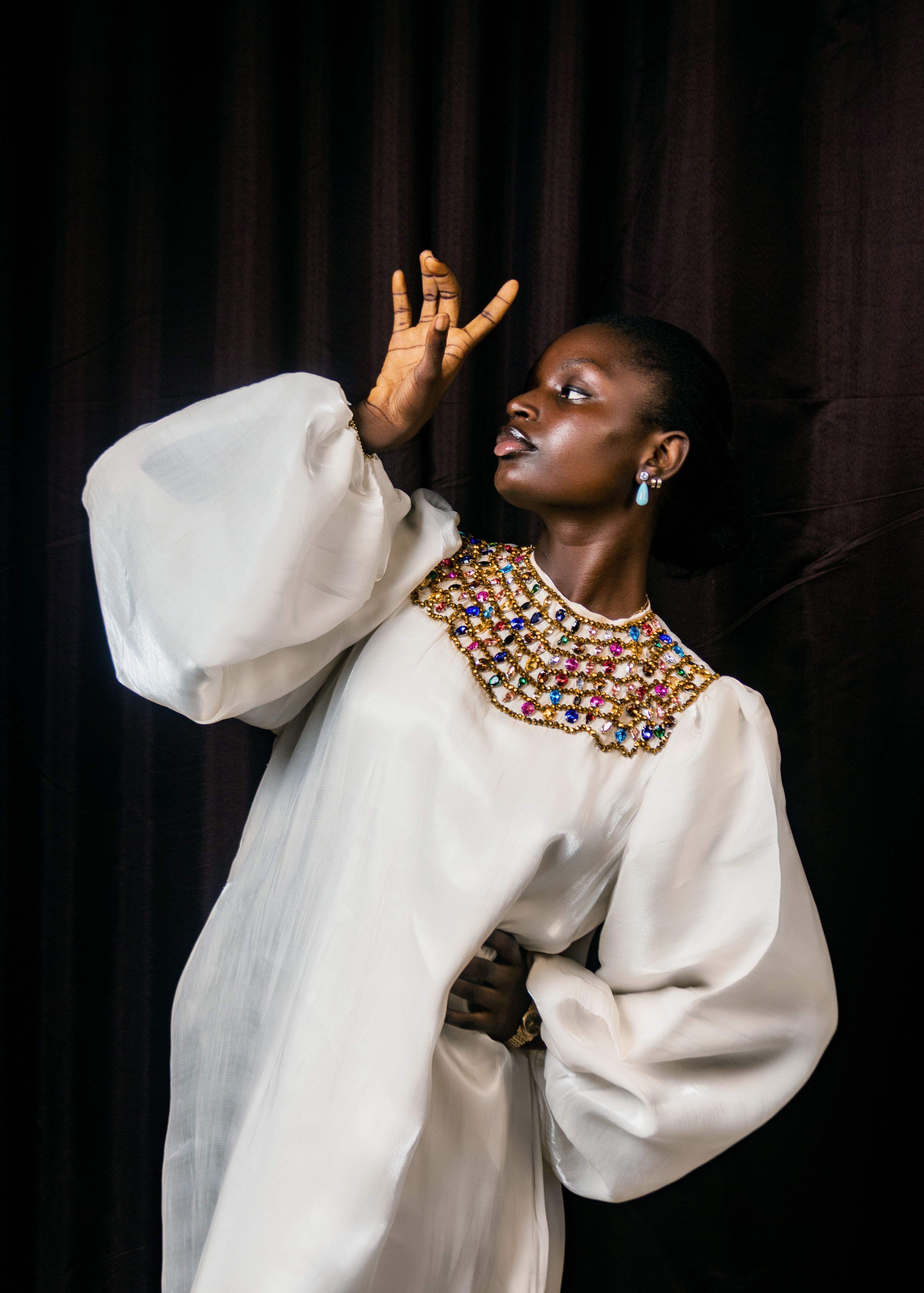 Stunning portrait of a woman in a white dress with colorful beads against a dark background.