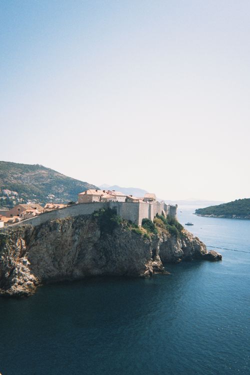 Free Breathtaking view of Dubrovnik's ancient city walls perched on a cliff above the tranquil Adriatic Sea. Stock Photo