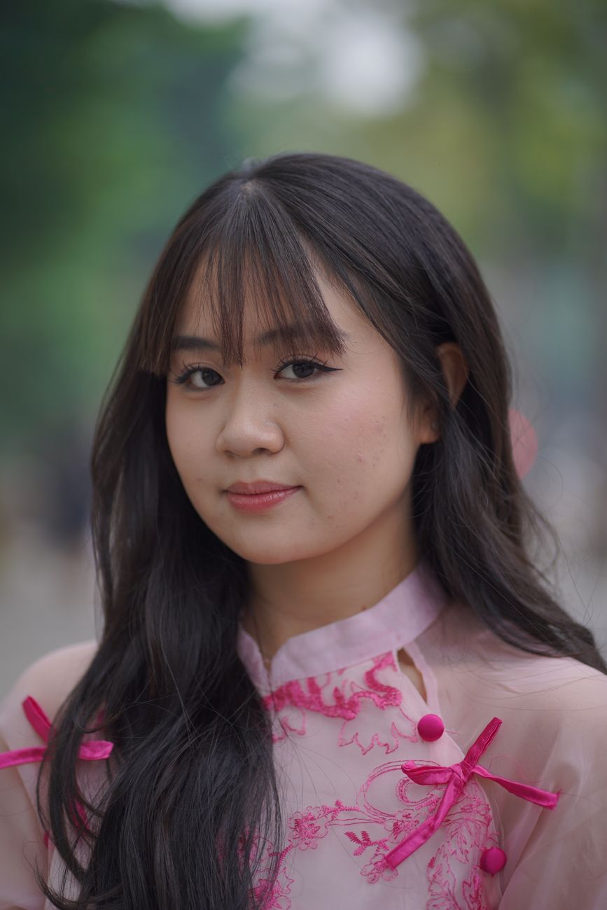 Close-up portrait of a woman in pink traditional Vietnamese dress outdoors.