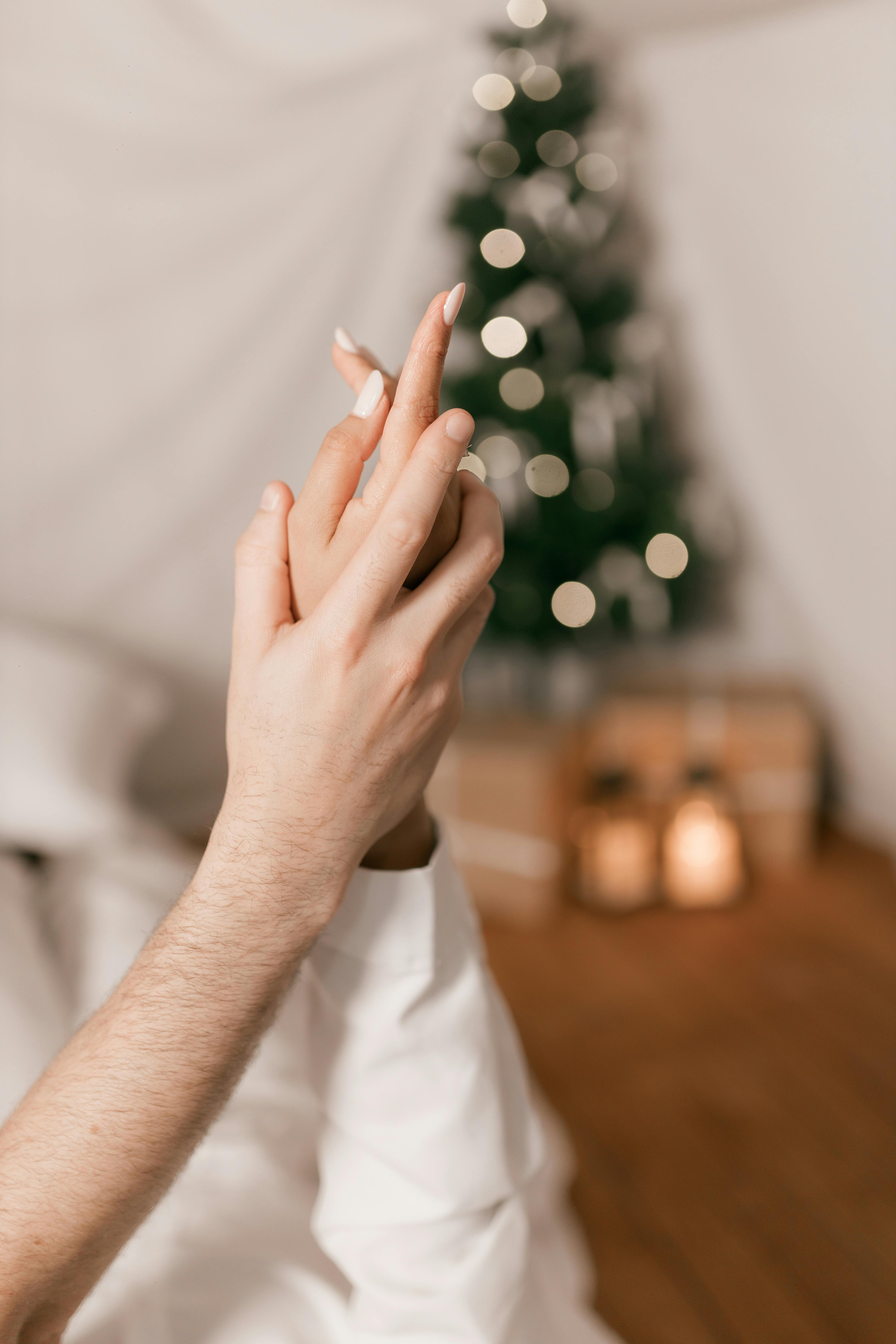 Close-up of a couple holding hands in front of a Christmas tree, creating a warm and festive atmosphere.