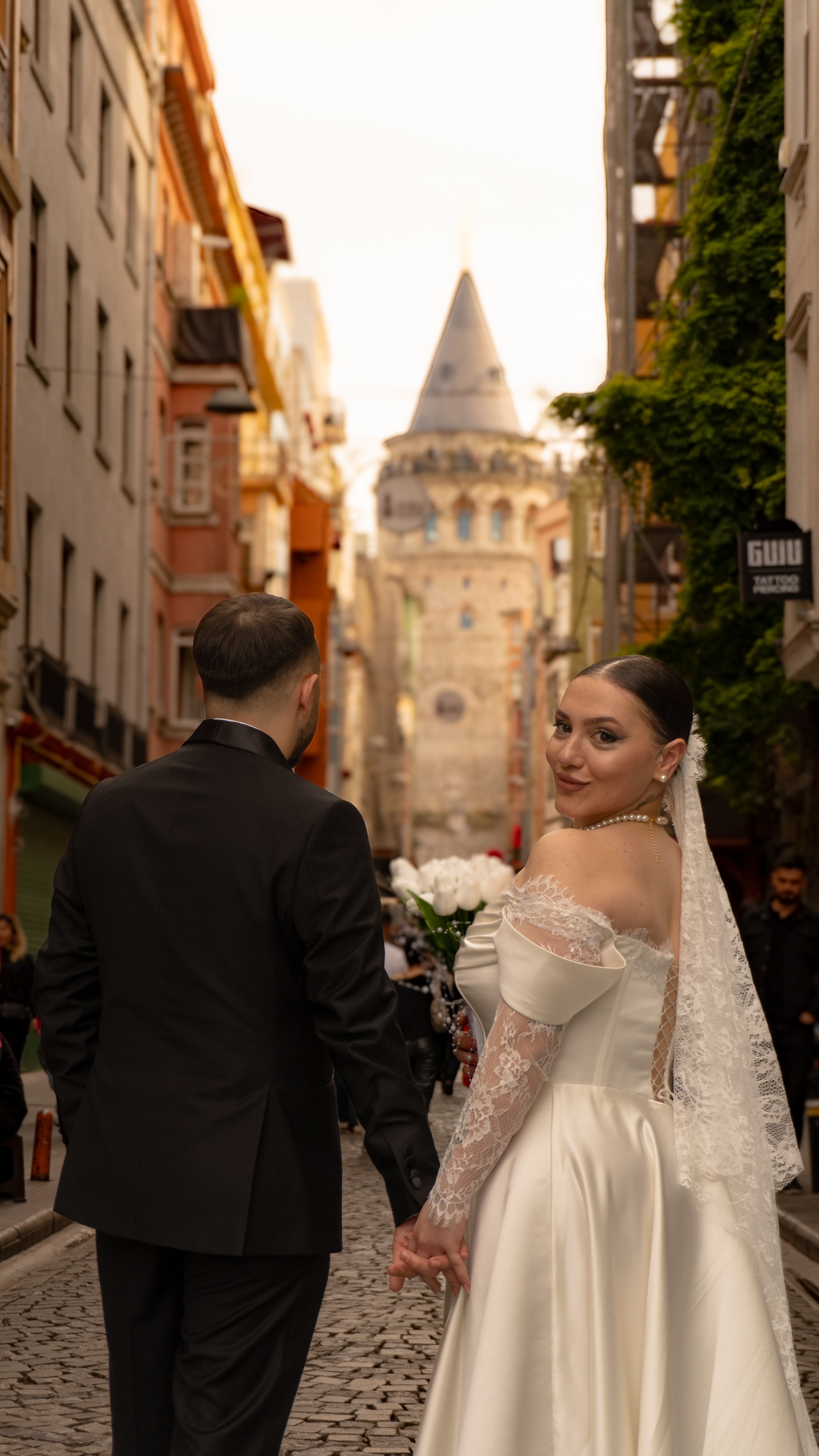 Bride and groom hold hands in front of the historic Galata Tower, embracing love in Istanbul.