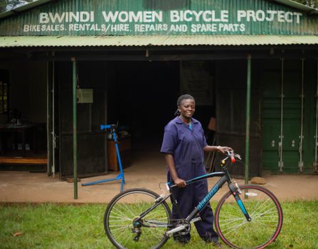 A woman stands proudly with a bicycle at Bwindi Women Bicycle Project. Empowerment and community development.