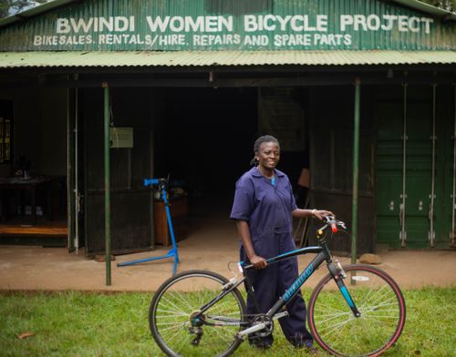 Free A woman stands proudly with a bicycle at Bwindi Women Bicycle Project. Empowerment and community development. Stock Photo
