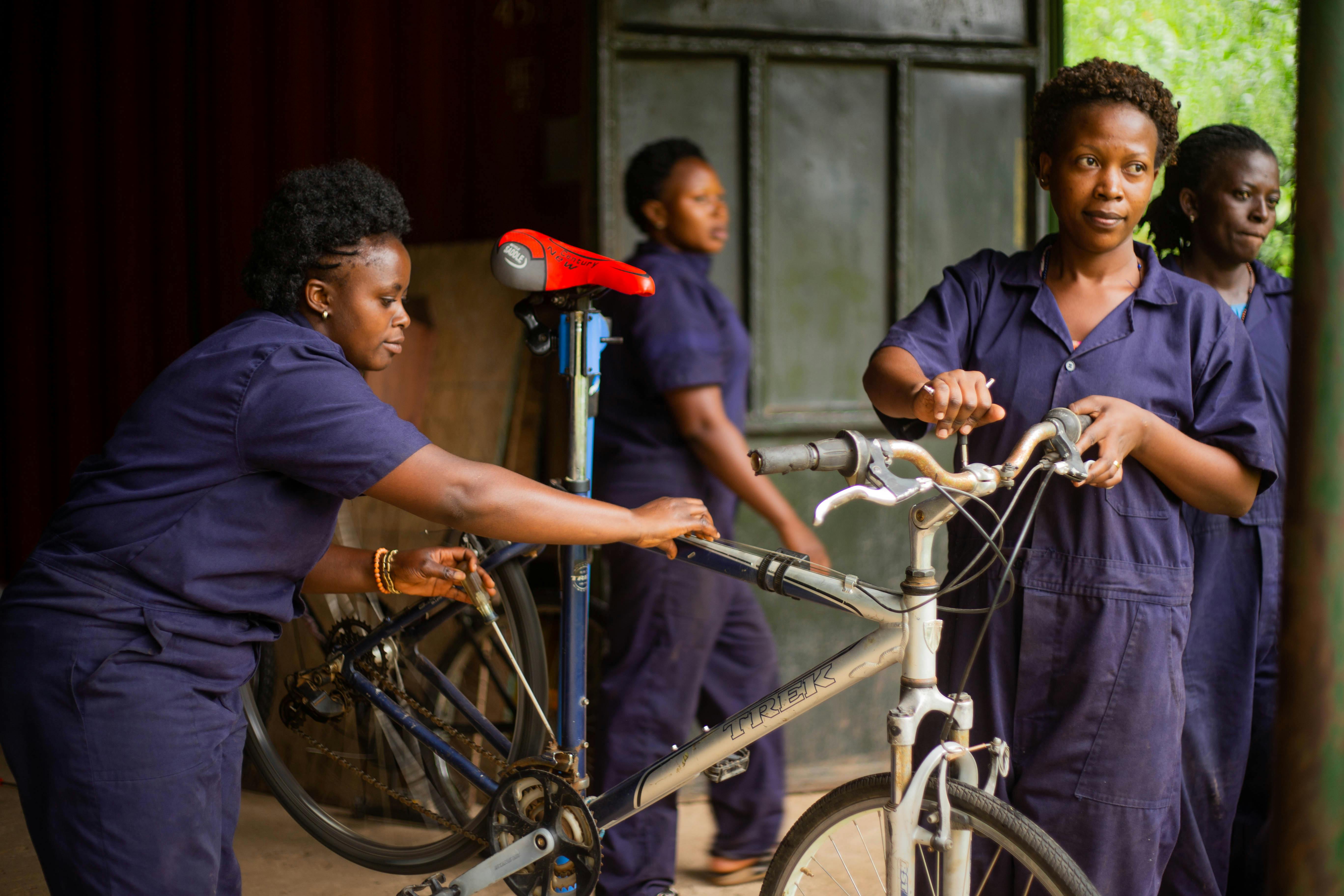 Women in uniforms fixing bicycles in an indoor workshop setting.