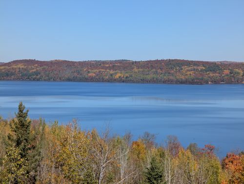 Free Peaceful autumn scene featuring a calm lake surrounded by colorful trees under a clear blue sky. Stock Photo