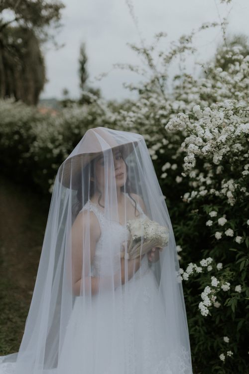 Free A bride in a bridal gown stands among lush white flowers, holding a bouquet. Stock Photo
