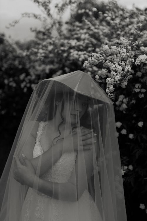 Free Elegant black and white portrait of a bride with a veil, surrounded by blooming flowers. Stock Photo