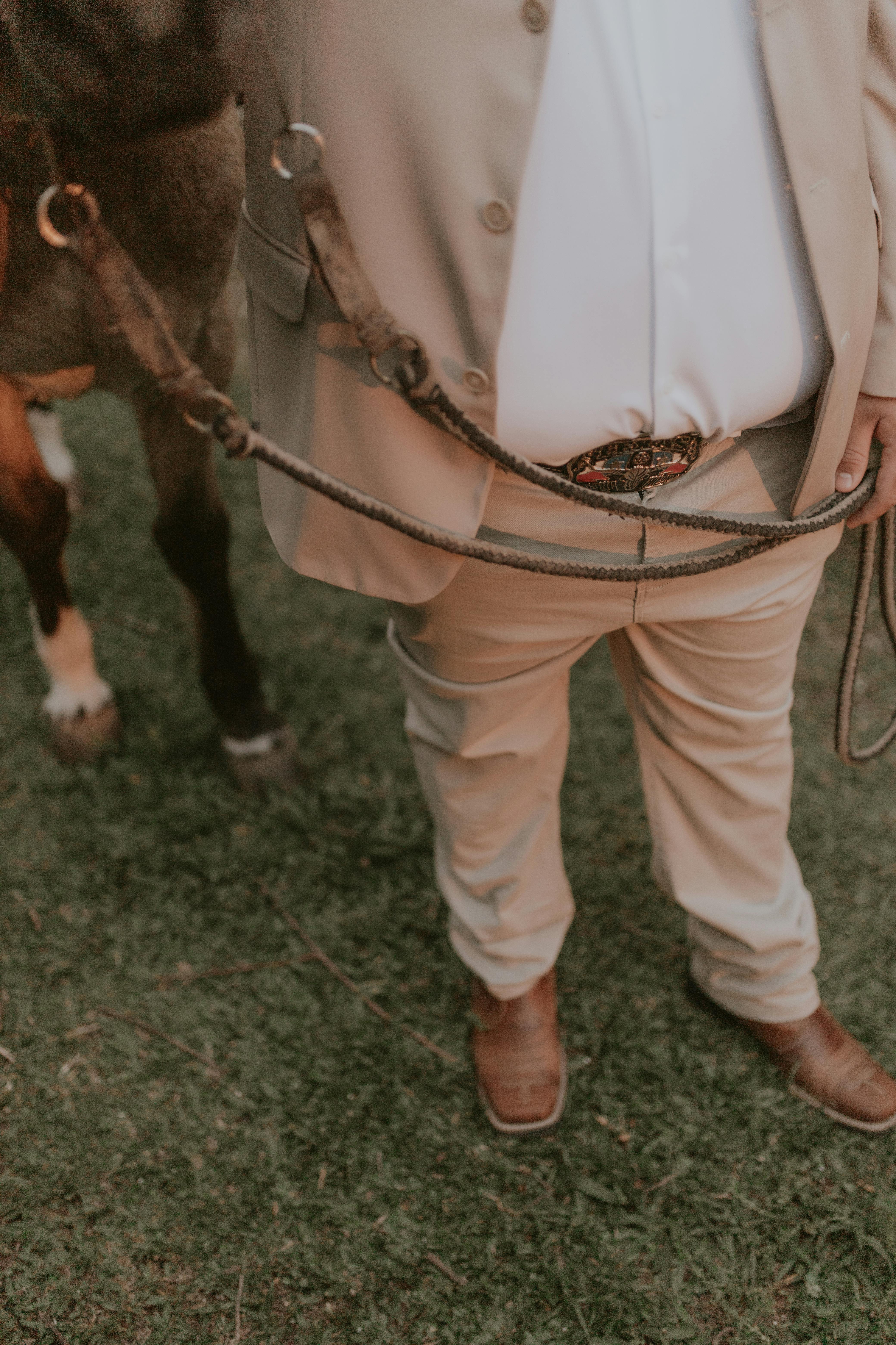 Man dressed in formal attire holding a horse lead outdoors on grass.