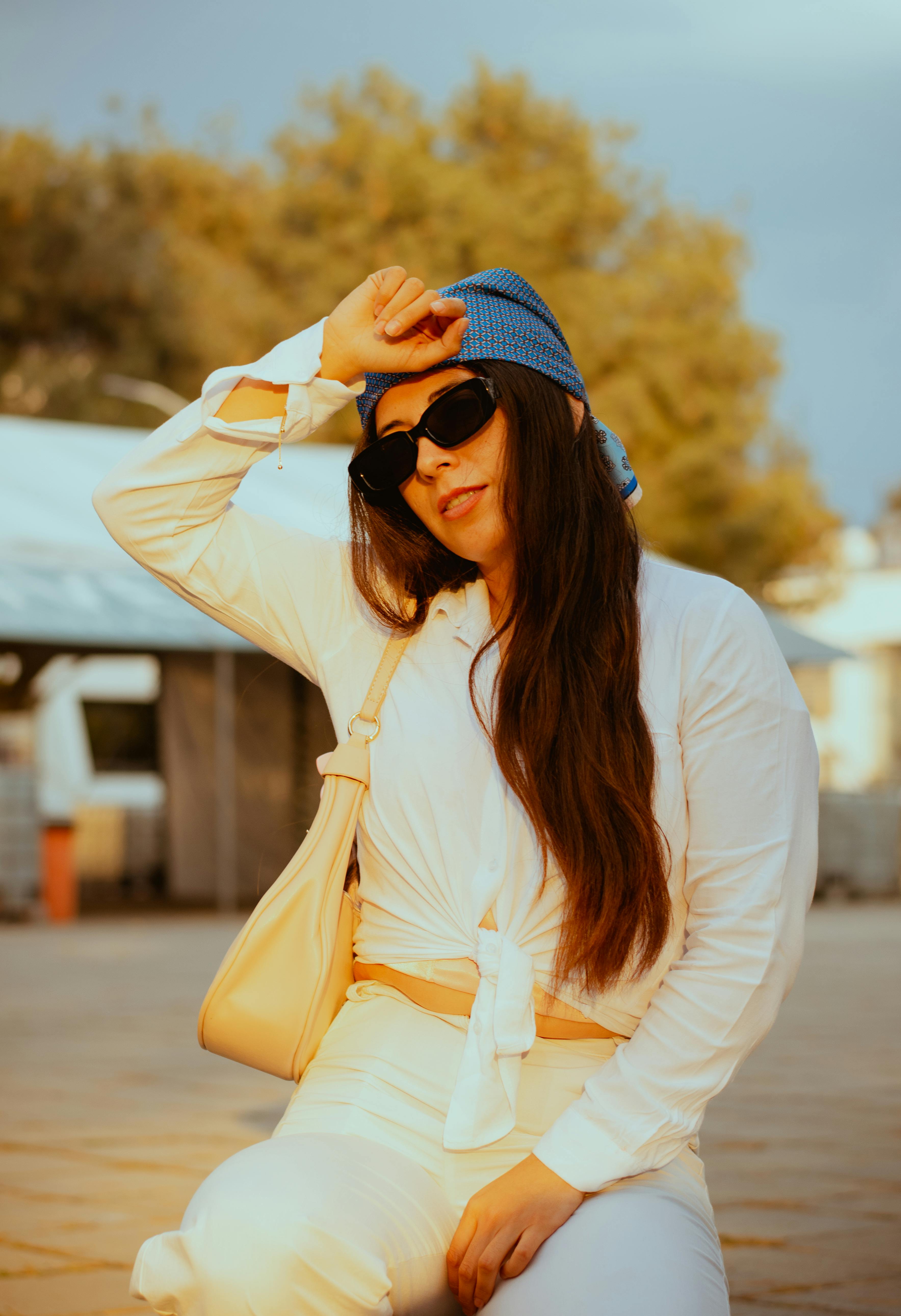 Fashionable woman in white outfit and sunglasses enjoying sunshine outdoors. Perfect for lifestyle and fashion themes.