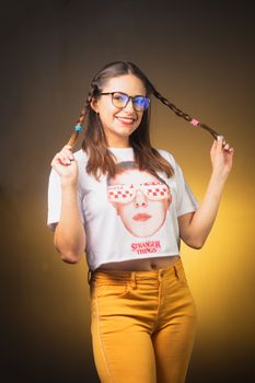 A cheerful woman playing with her braids, wearing a graphic tee and bright pants.