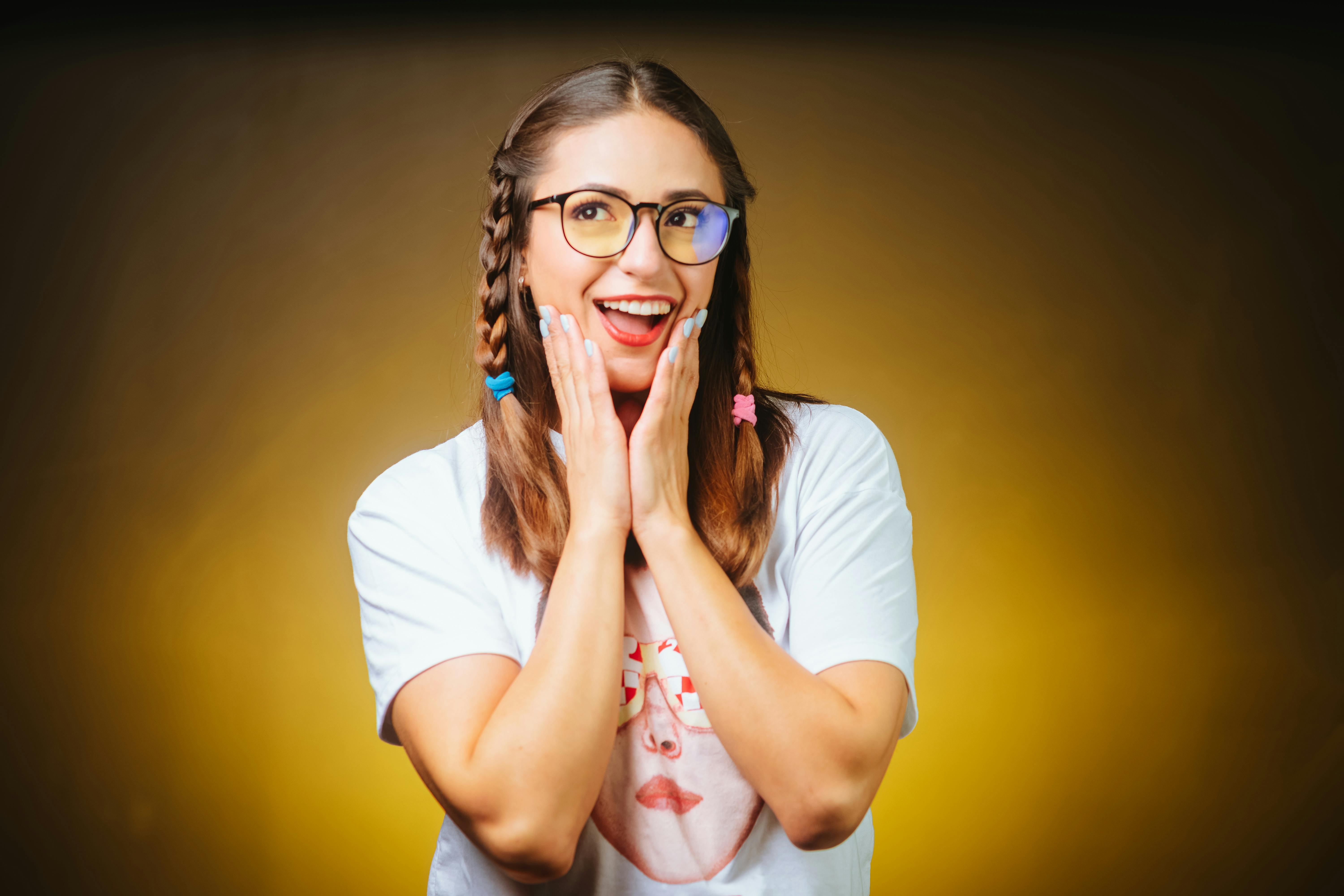 Miễn phí Một người phụ nữ vui vẻ với mái tóc tết và đeo kính đang thể hiện sự ngạc nhiên trên nền màu vàng rực rỡ. Ảnh lưu trữ