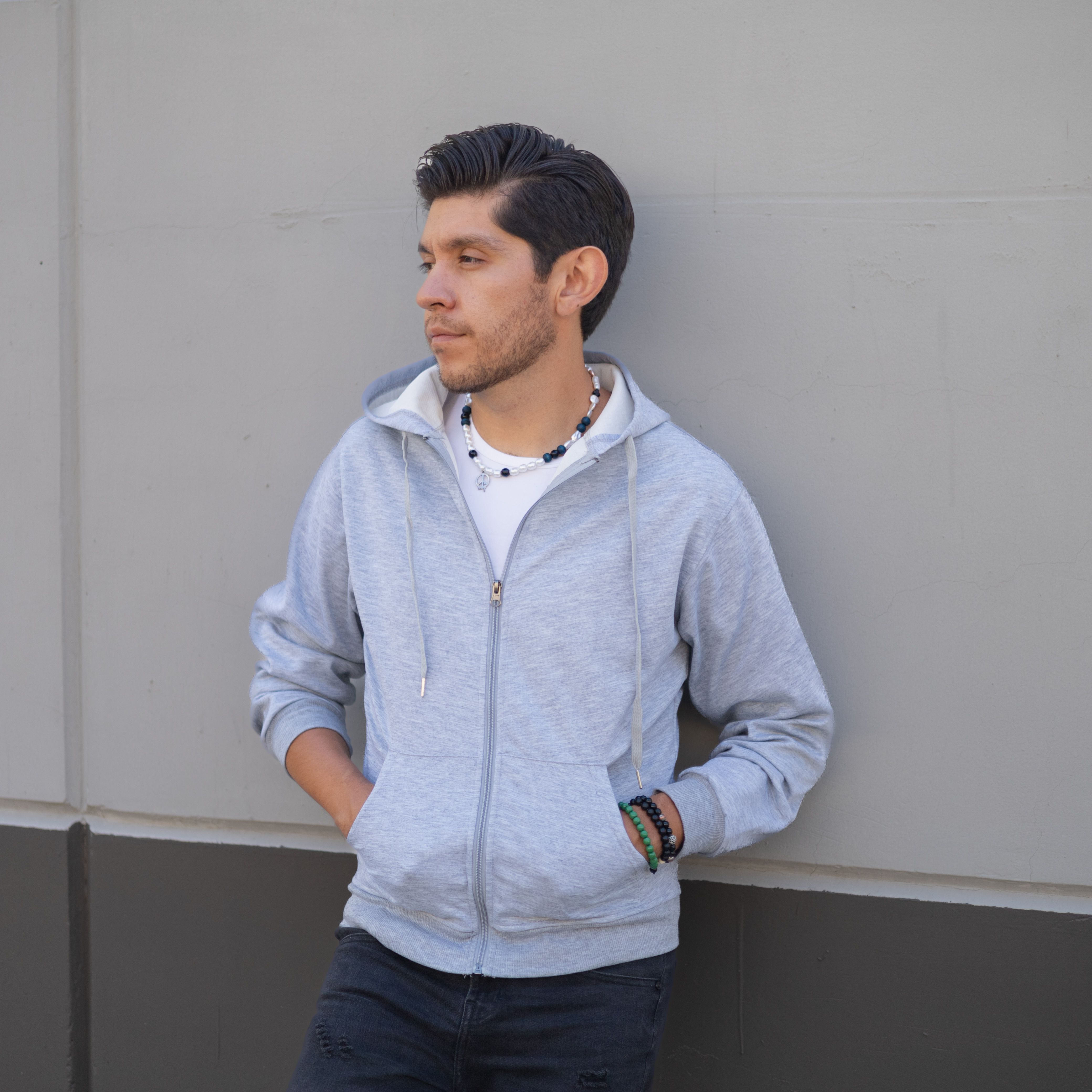 Man in a pale heather full-zip hoodie leaning against a concrete wall — photo by Luiz Ramírez on Pexels