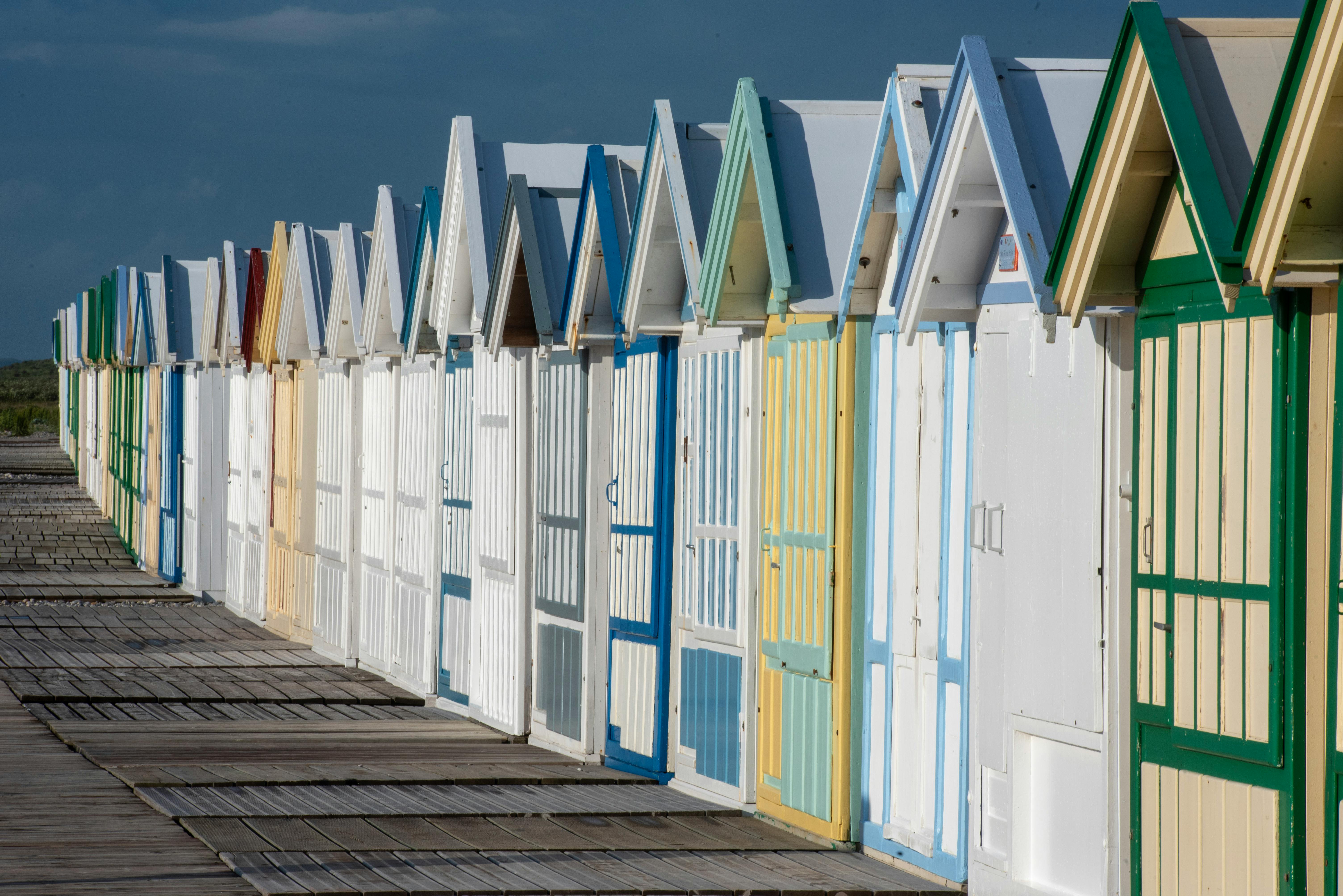 Vivid row of colorful beach huts along a wooden boardwalk, capturing summer vibes.