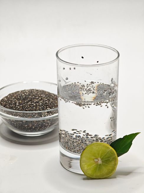 Top 9 công dụng của hạt é với sức khỏe 2 Glass of chia seed water with a lime slice and bowl of seeds on white surface.