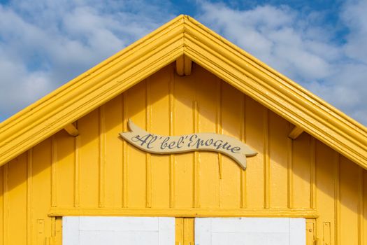 Vibrant yellow wooden cabin facade with a sign reading 'Al' bel' Epoque' under a blue sky.
