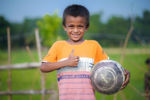 A cheerful young boy gives a thumbs up holding a soccer ball in a lush outdoor setting.