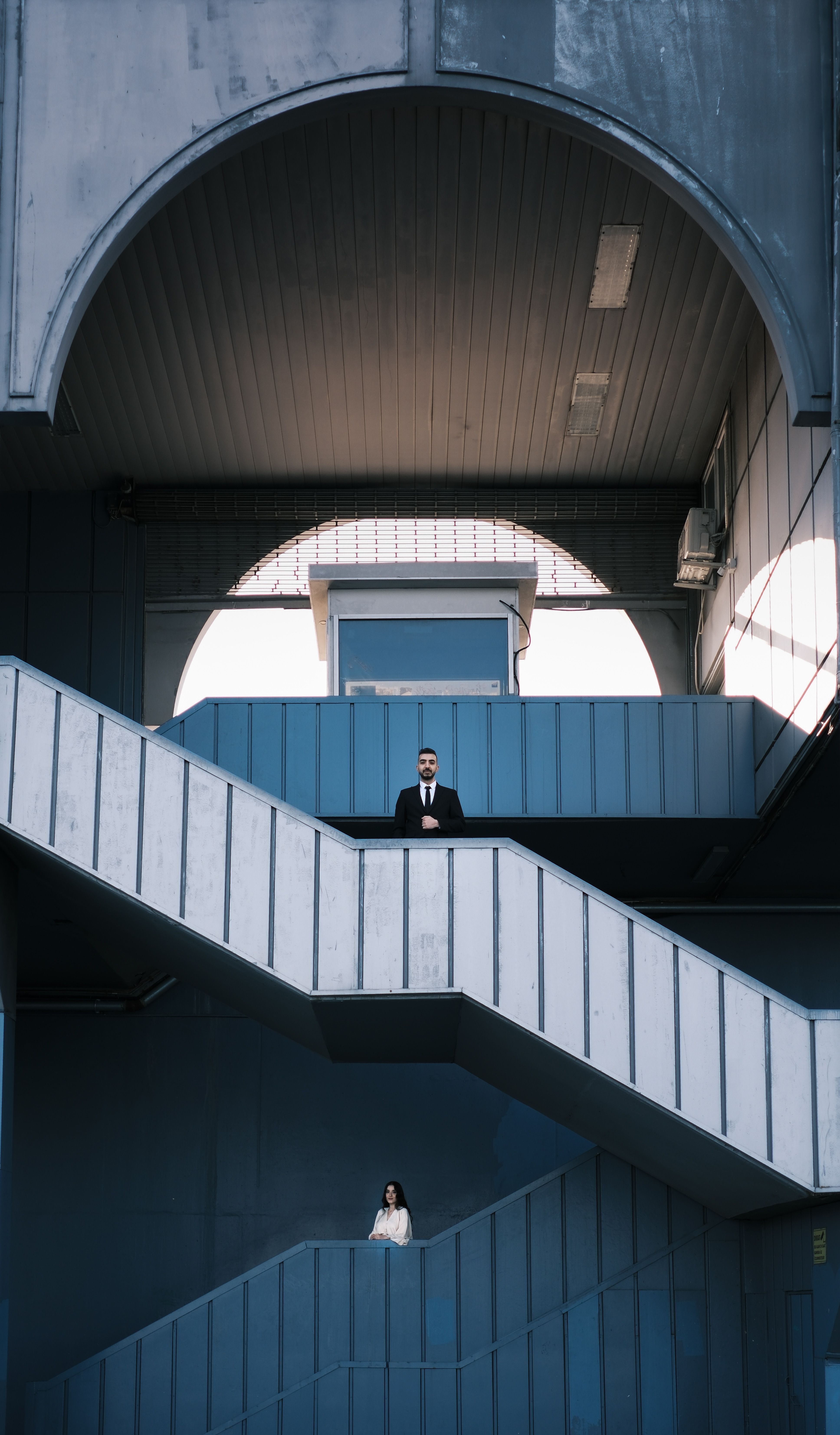 Two individuals in formal attire on a modern staircase in an architectural setting.