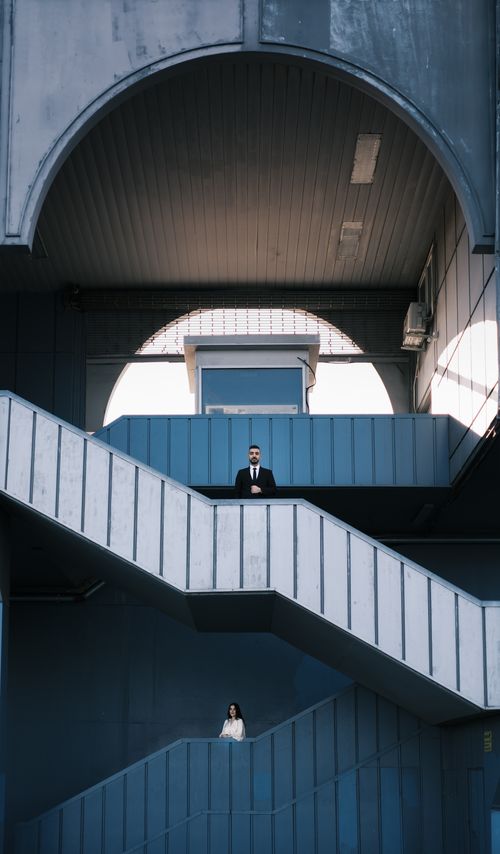 Free Two individuals in formal attire on a modern staircase in an architectural setting. Stock Photo