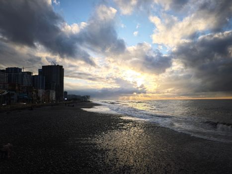 Sunset over a pebble beach with dramatic clouds and city skyline, perfect for coastal and urban themes.