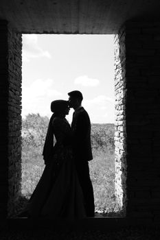Silhouette of an embracing couple framed by a stone archway with outdoor background.