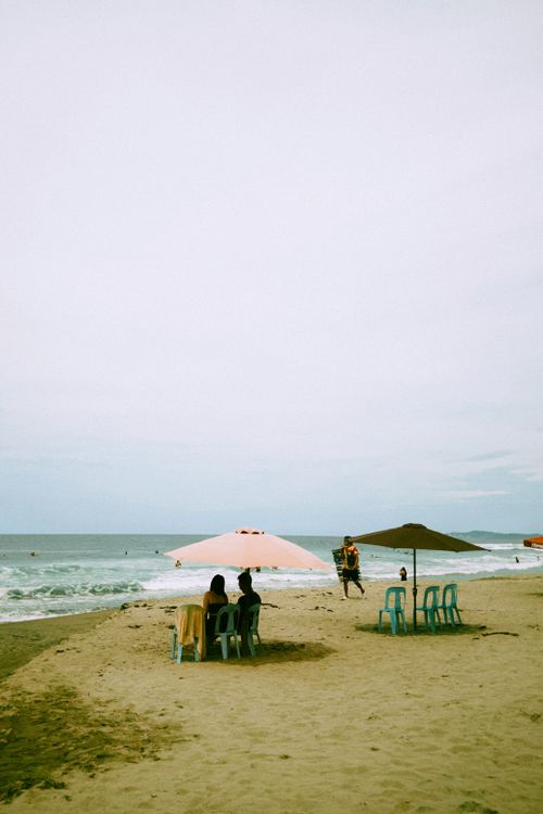 Free Tranquil beach scene with umbrellas and people enjoying leisure time on sandy shores. Stock Photo