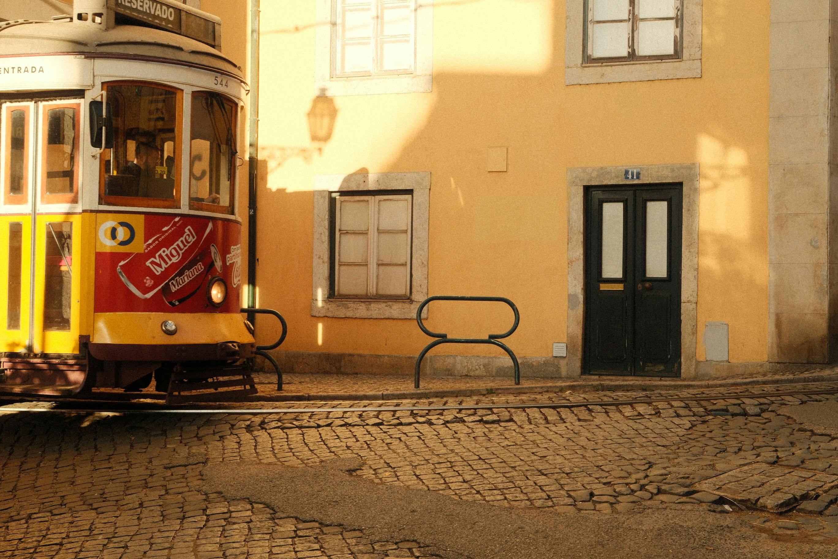 Classic Lisbon tram passing by a colorful building on sunny cobblestone streets.
