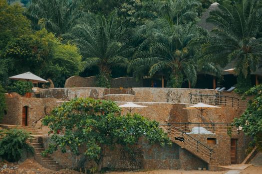 Luxurious stone resort nestled in lush tropical greenery with palm trees and umbrellas, offering a tranquil escape.