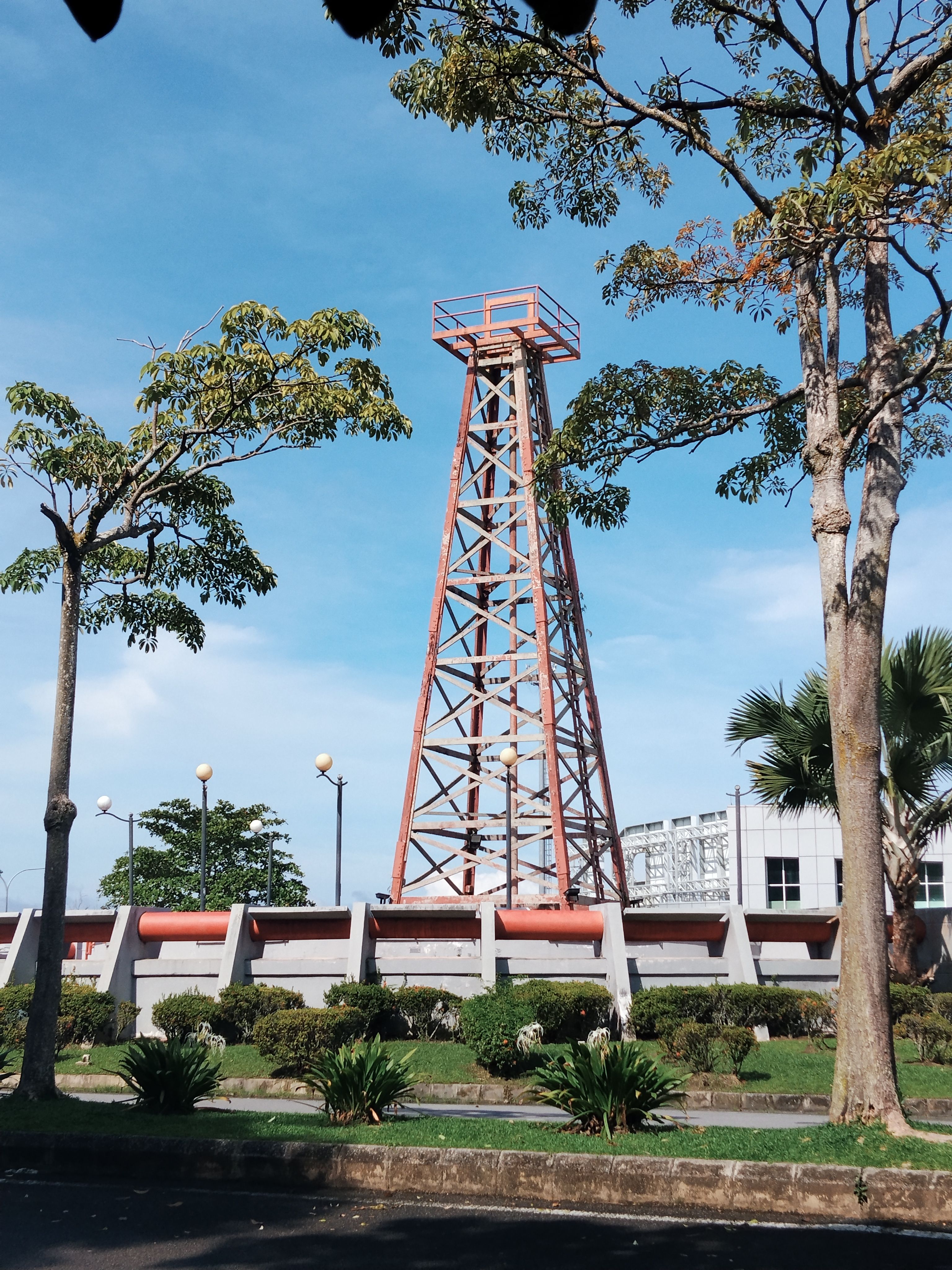 Historic oil derrick tower surrounded by trees in Miri, Sarawak, Malaysia under clear blue sky.