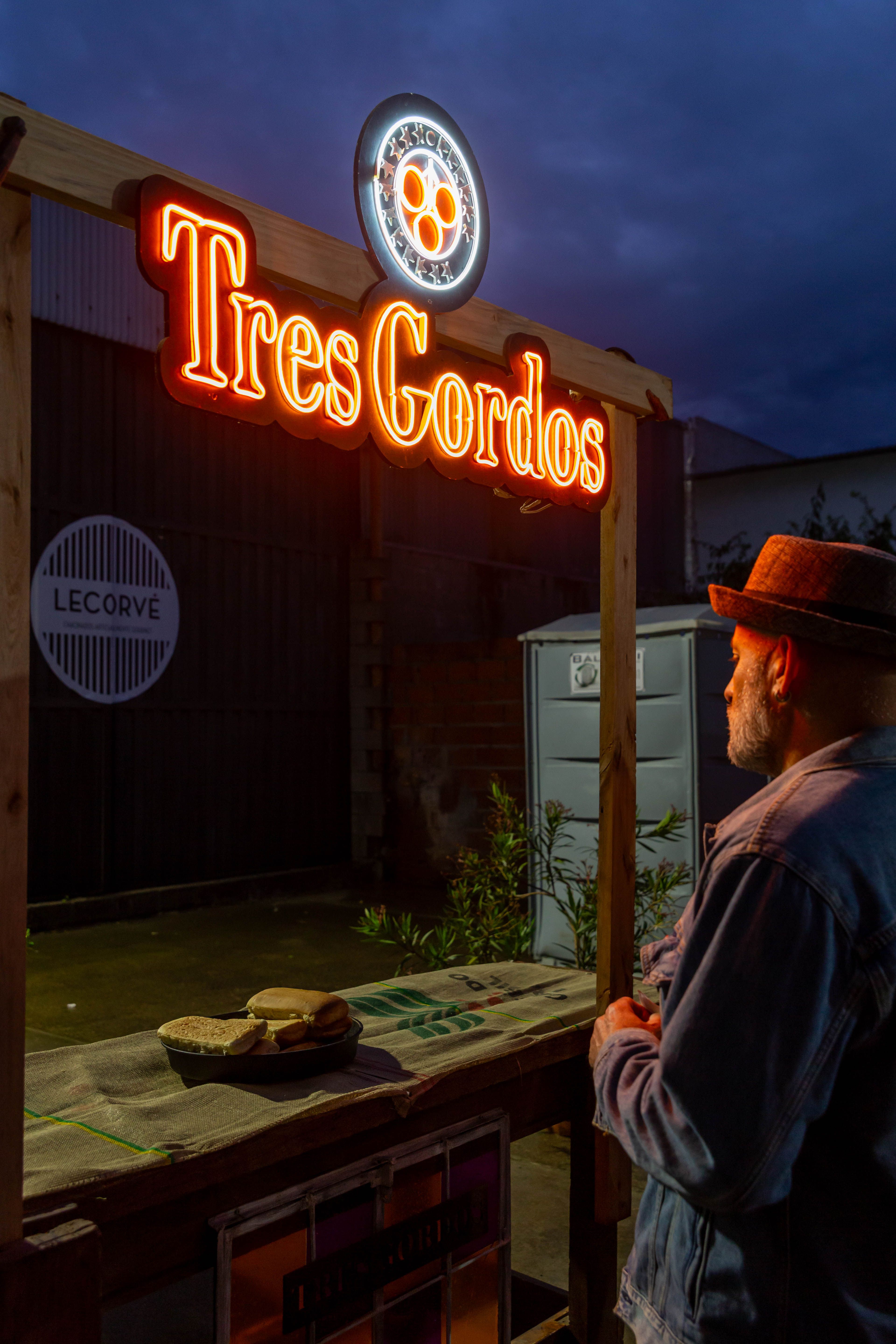 A man stands at a vibrant night market stand named Tres Gordos in Mar del Plata.