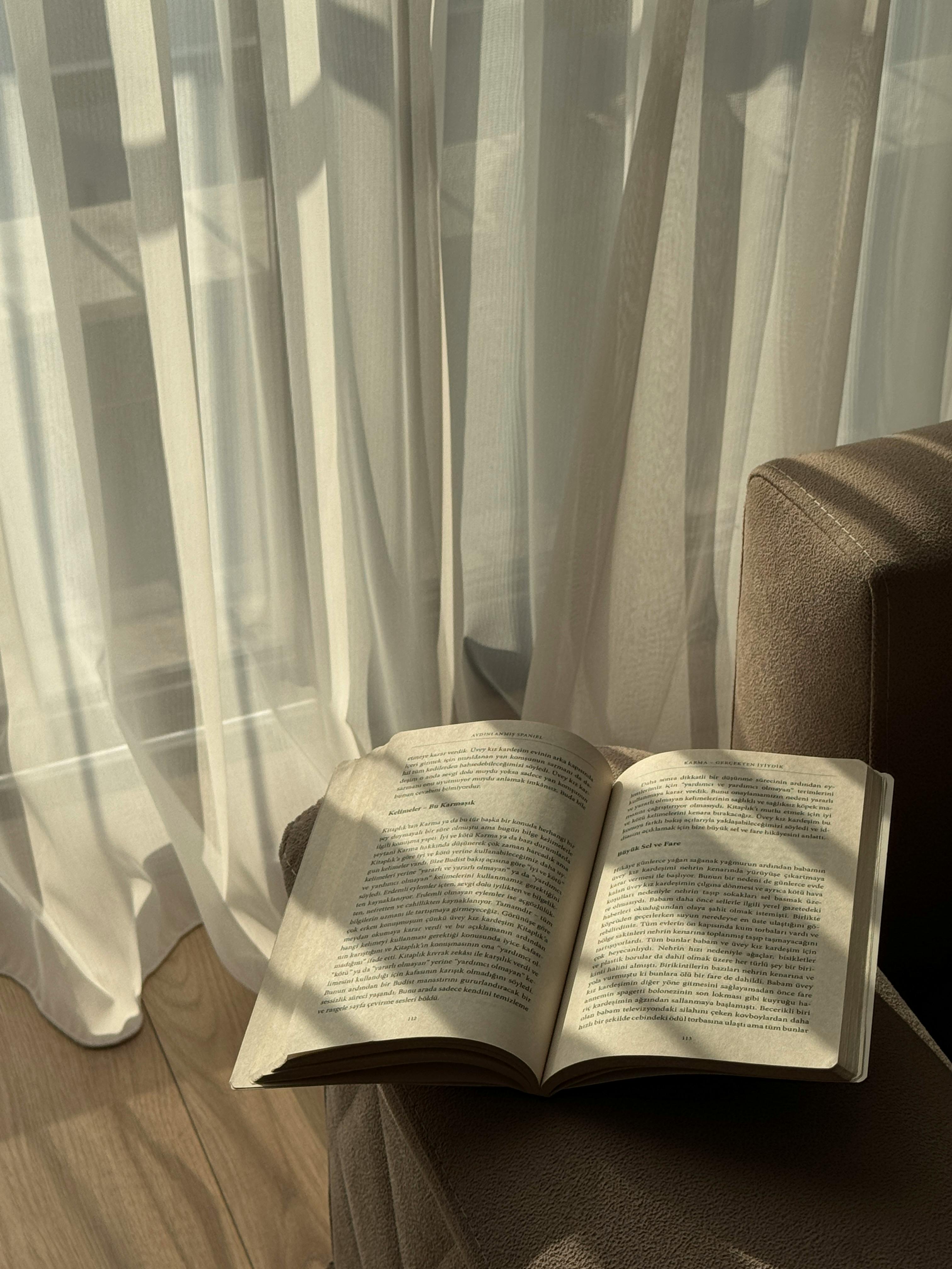 A tranquil reading spot with a book and soft sunlight casting shadows through curtains in İzmir, Türkiye.