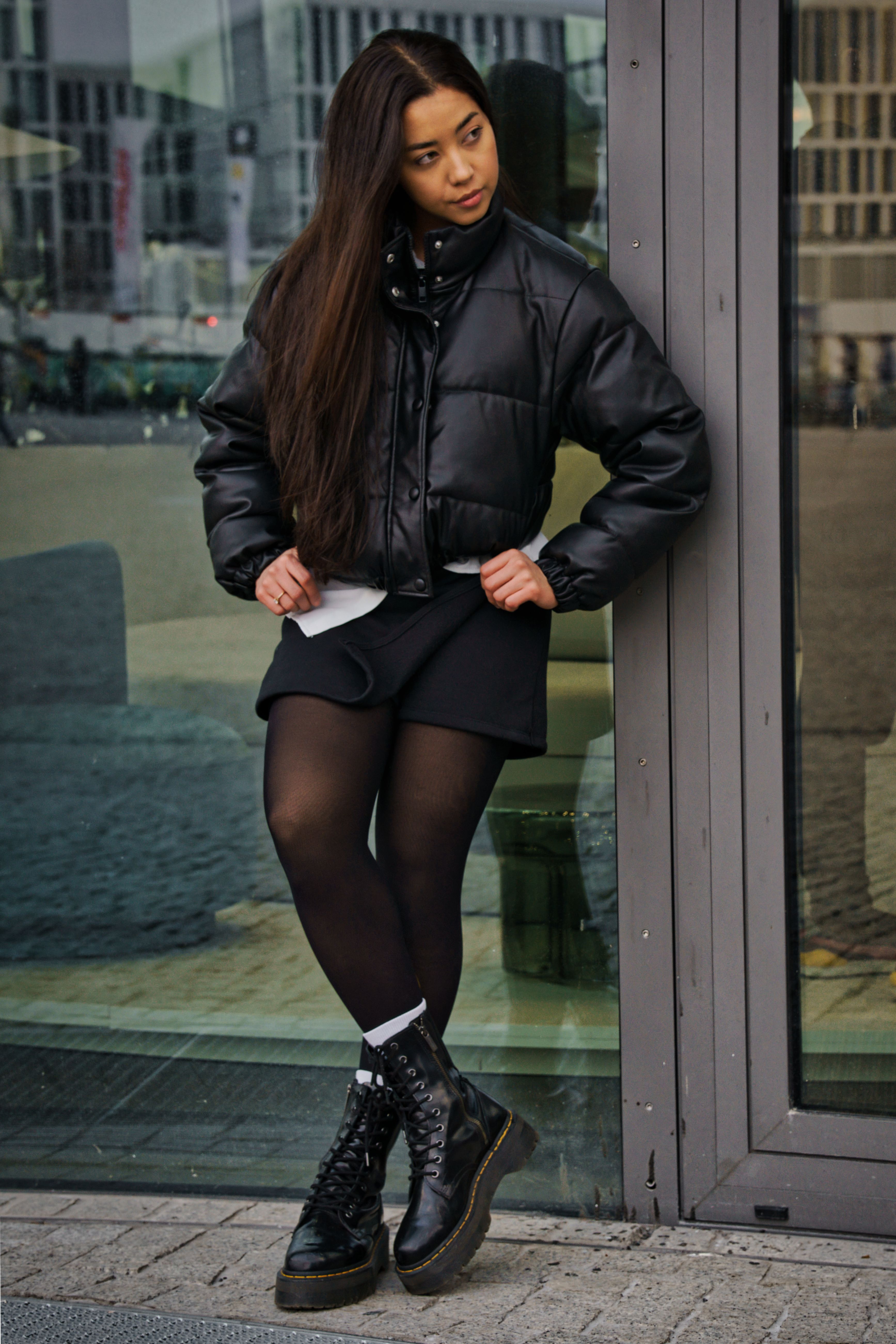 Young woman in fashionable attire leaning against a glass door in Berlin.