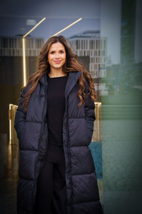 Free A young woman in a stylish black coat stands confidently against a modern urban backdrop in Berlin. Stock Photo