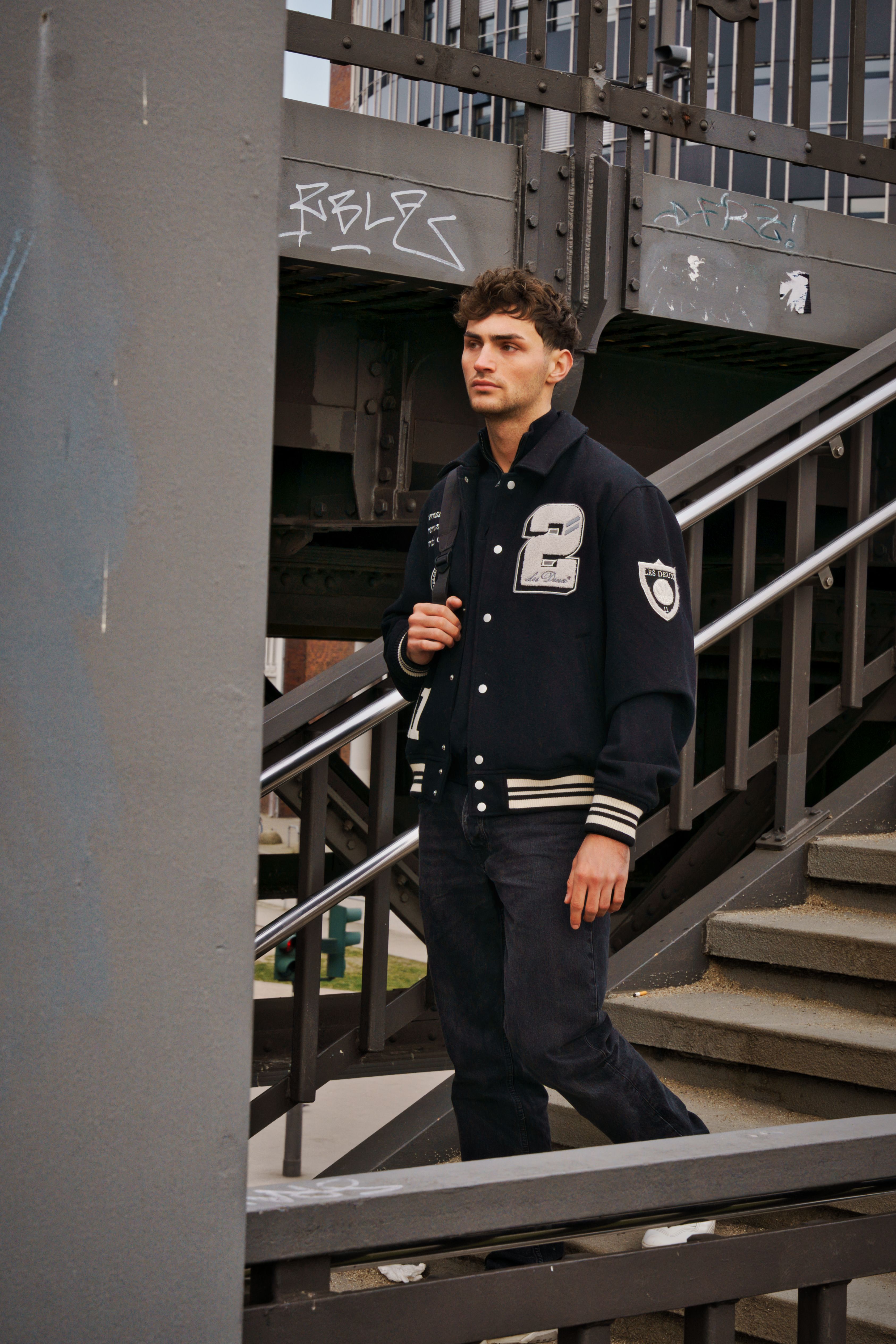 Stylish man in a varsity jacket descends an urban staircase in Hamburg, Germany.