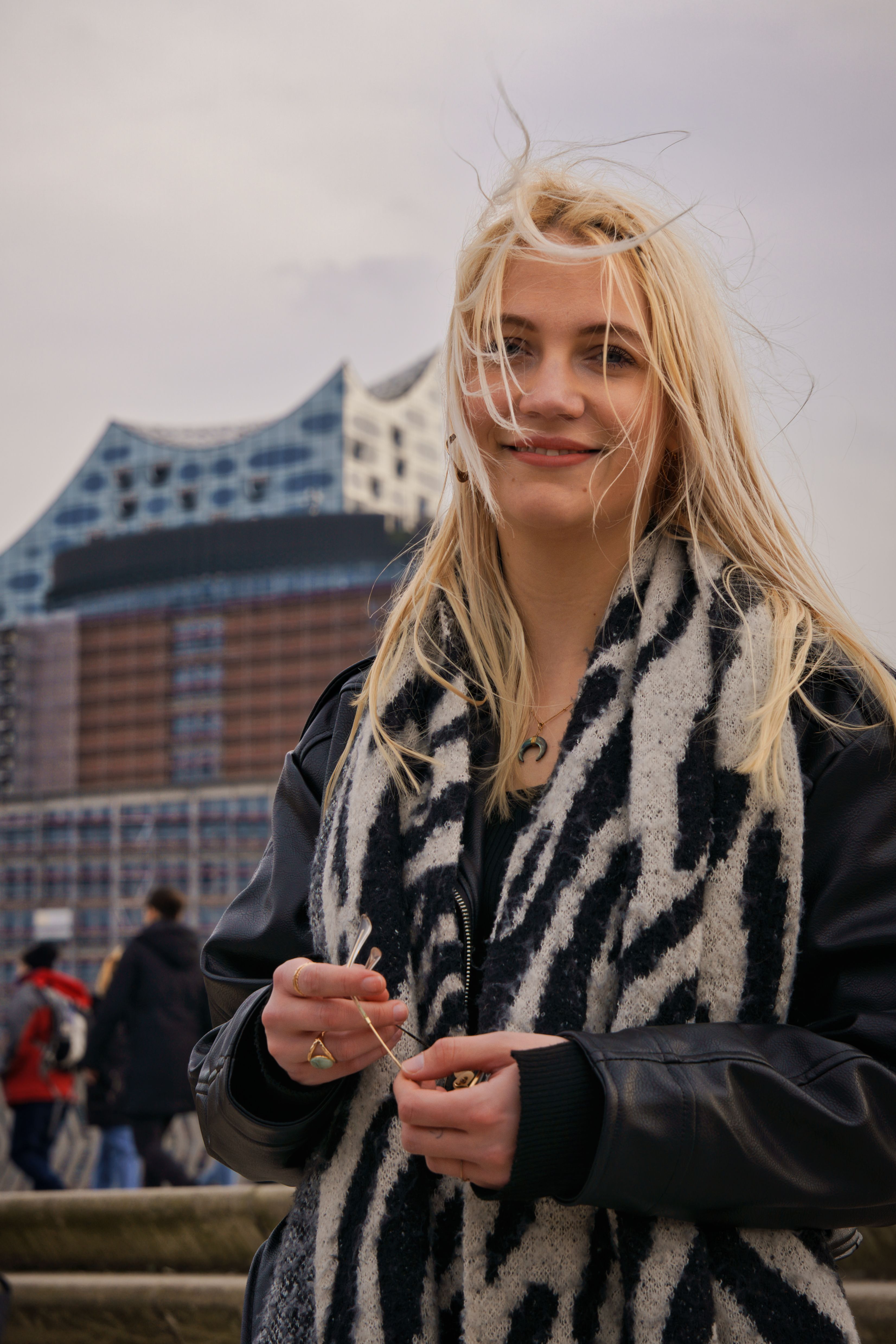 Portrait of a smiling woman outdoors in Hamburg with Elbphilharmonie in the background.
