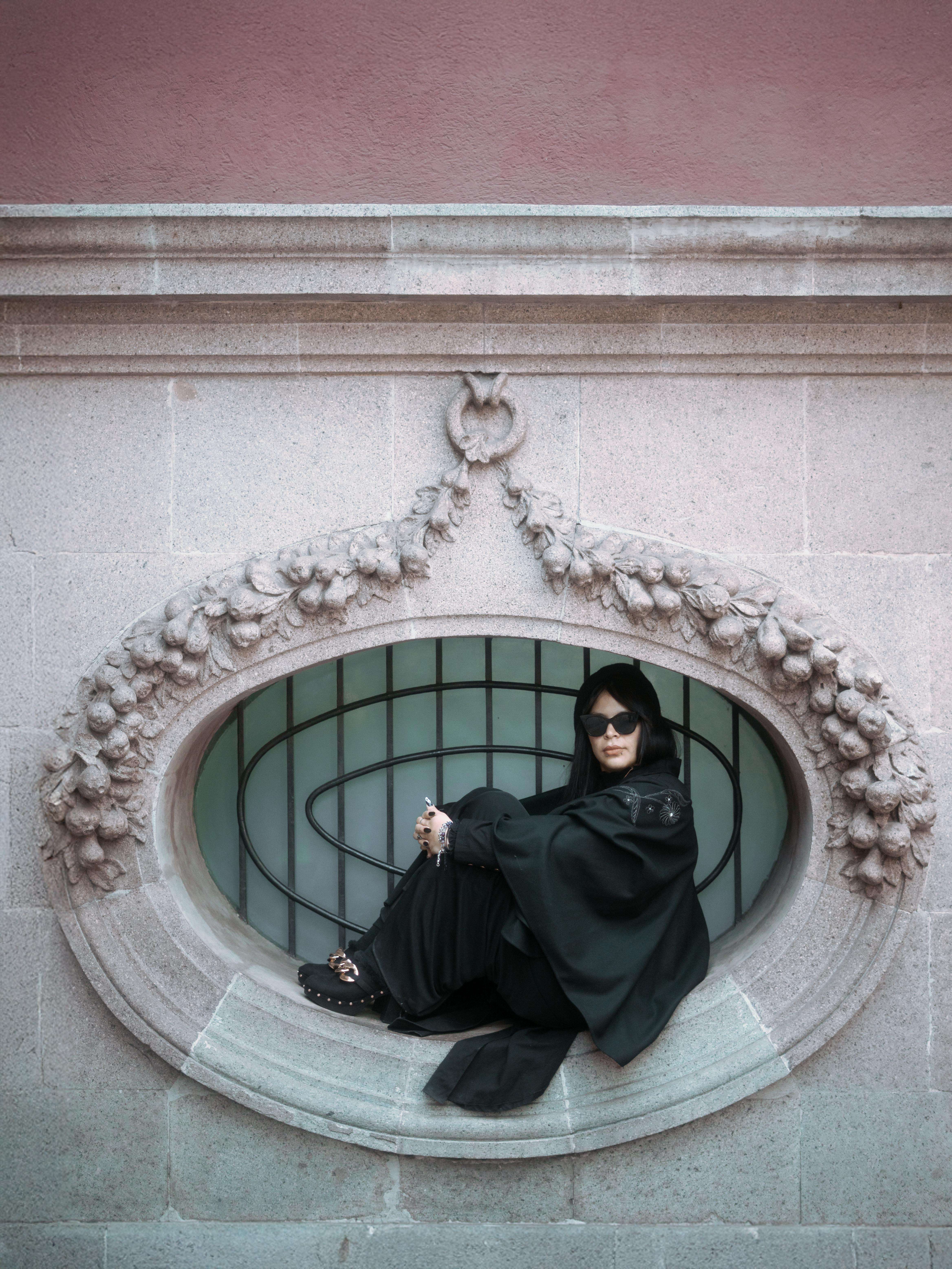 Gratis Elegante retrato de una mujer vestida de negro sentada en una ventana ornamentada en la Ciudad de México. Foto de stock