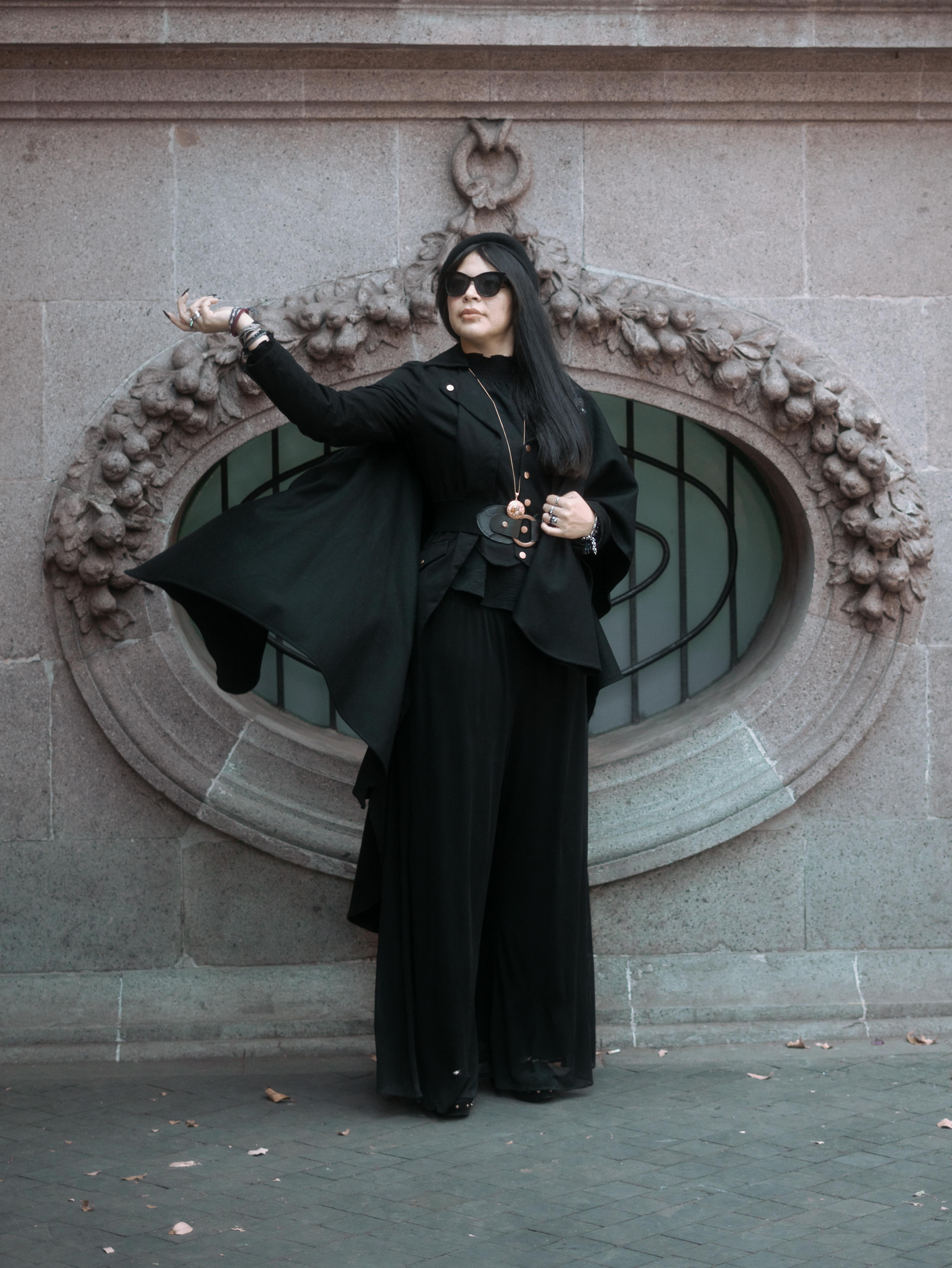 Gratis Una donna alla moda in abito nero posa con eleganza su uno sfondo classico in pietra a Città del Messico. Foto a disposizione