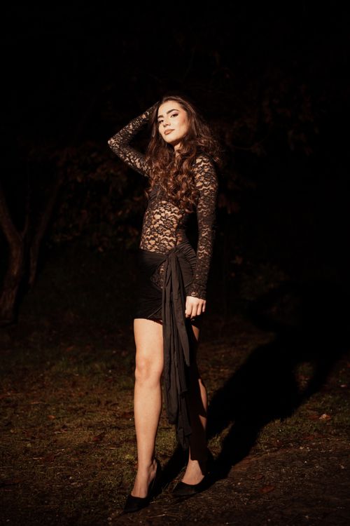 Free A young woman poses elegantly in a black lace dress during a nighttime outdoor photo shoot. Stock Photo