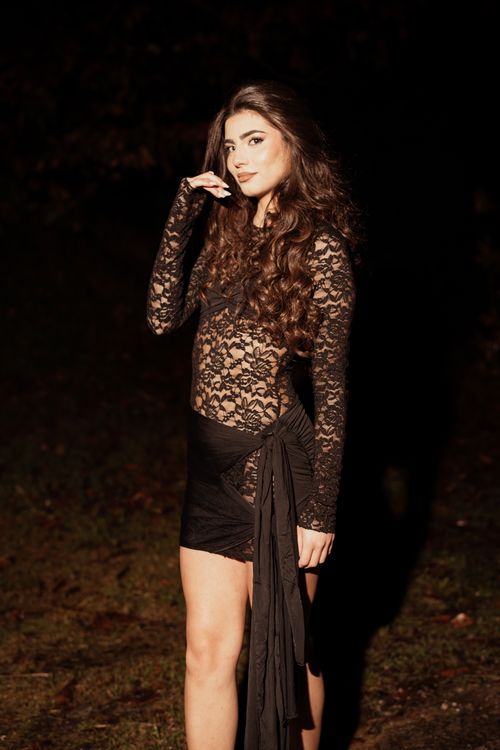 Free Portrait of a stylish woman in a lace dress posing outdoors at night, exuding glamor and elegance. Stock Photo