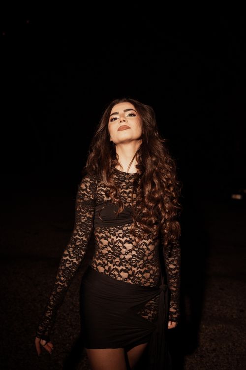 Free A stylish woman in a black lace dress poses outdoors at night, exuding confidence. Stock Photo