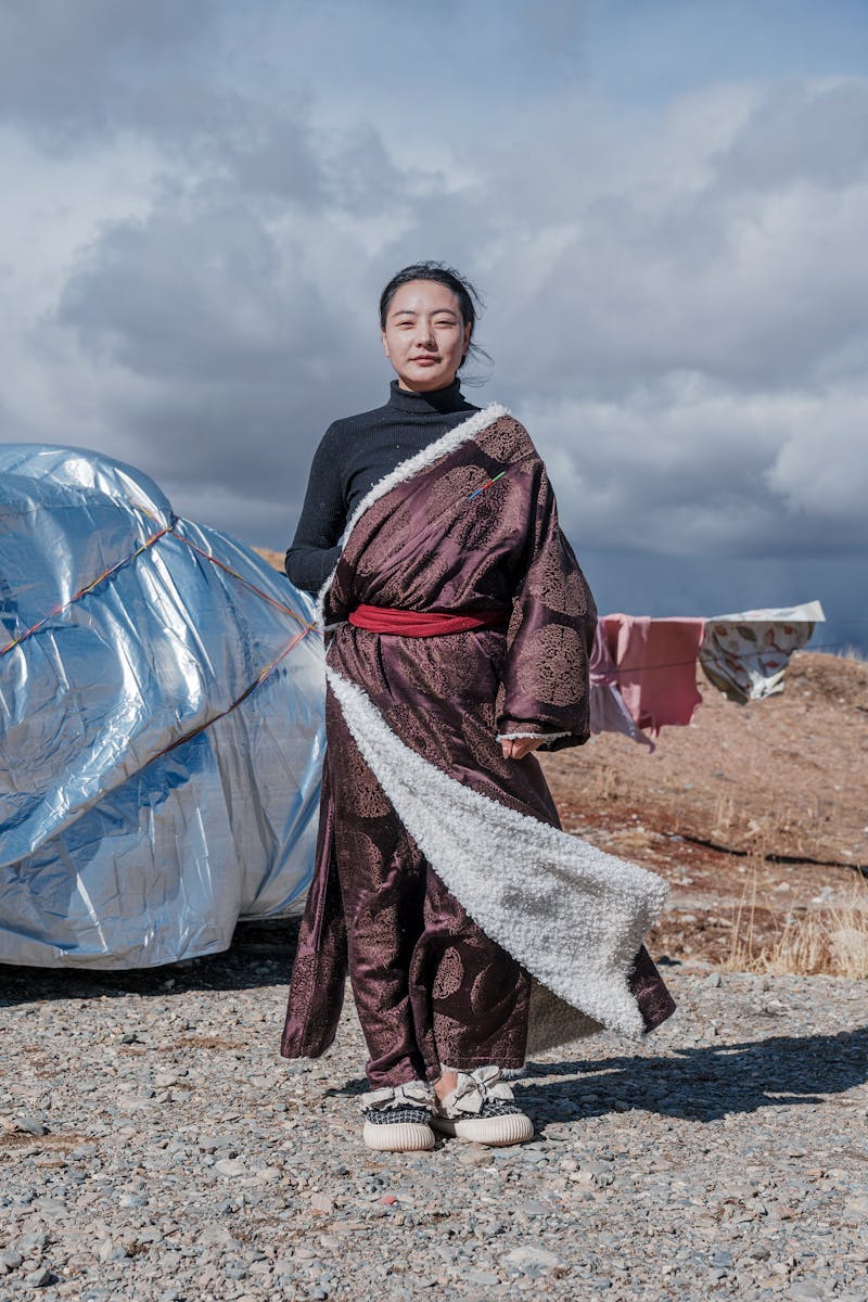 Woman in traditional robe standing outdoors, cloudy sky background, cultural expression.