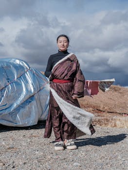 Woman in traditional robe standing outdoors, cloudy sky background, cultural expression.
