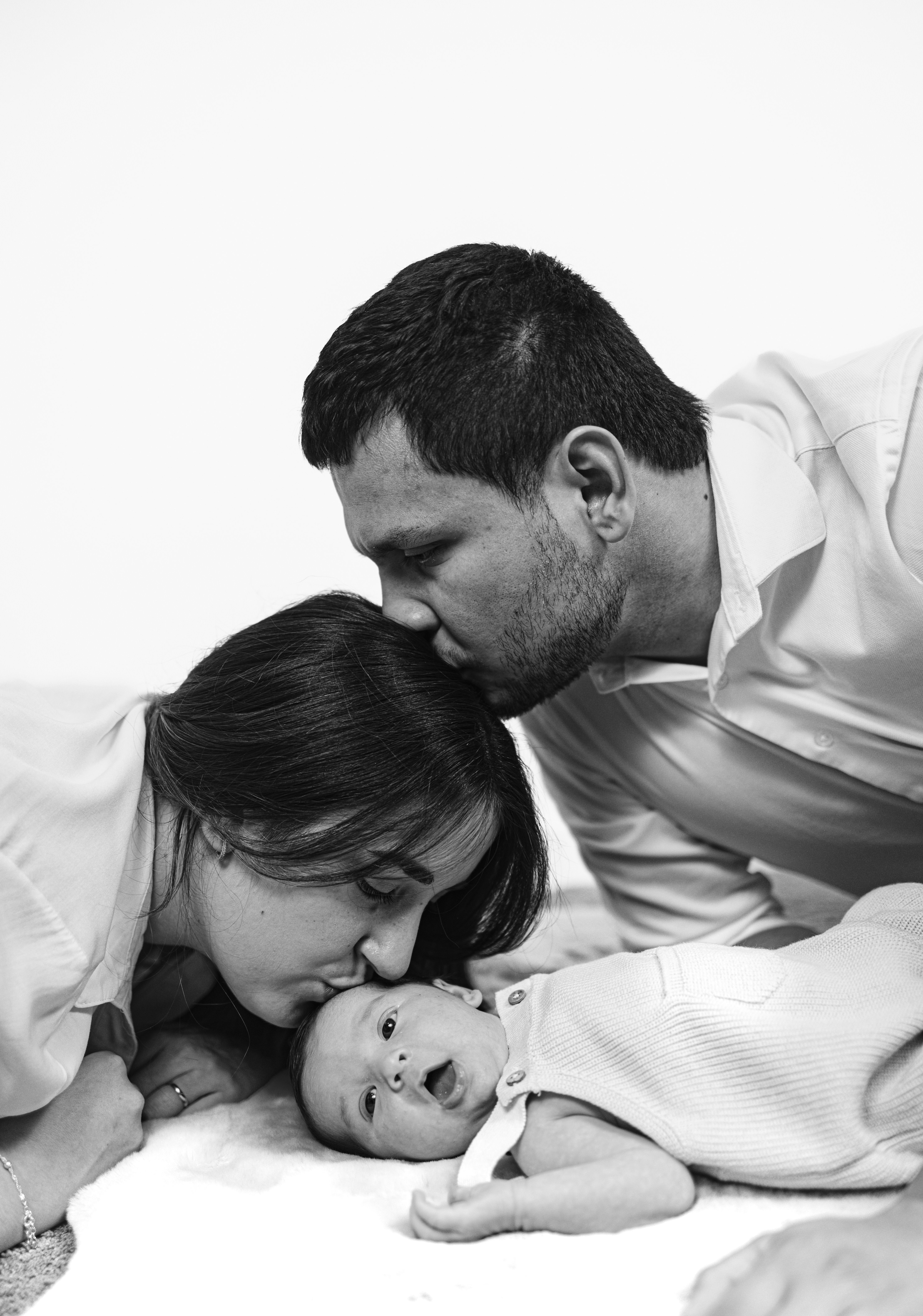 A loving family moment captured with parents kissing their newborn baby.
