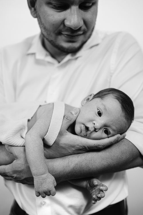 Free A touching black and white portrait of a father gently cradling his newborn baby, showcasing tender parenthood. Stock Photo