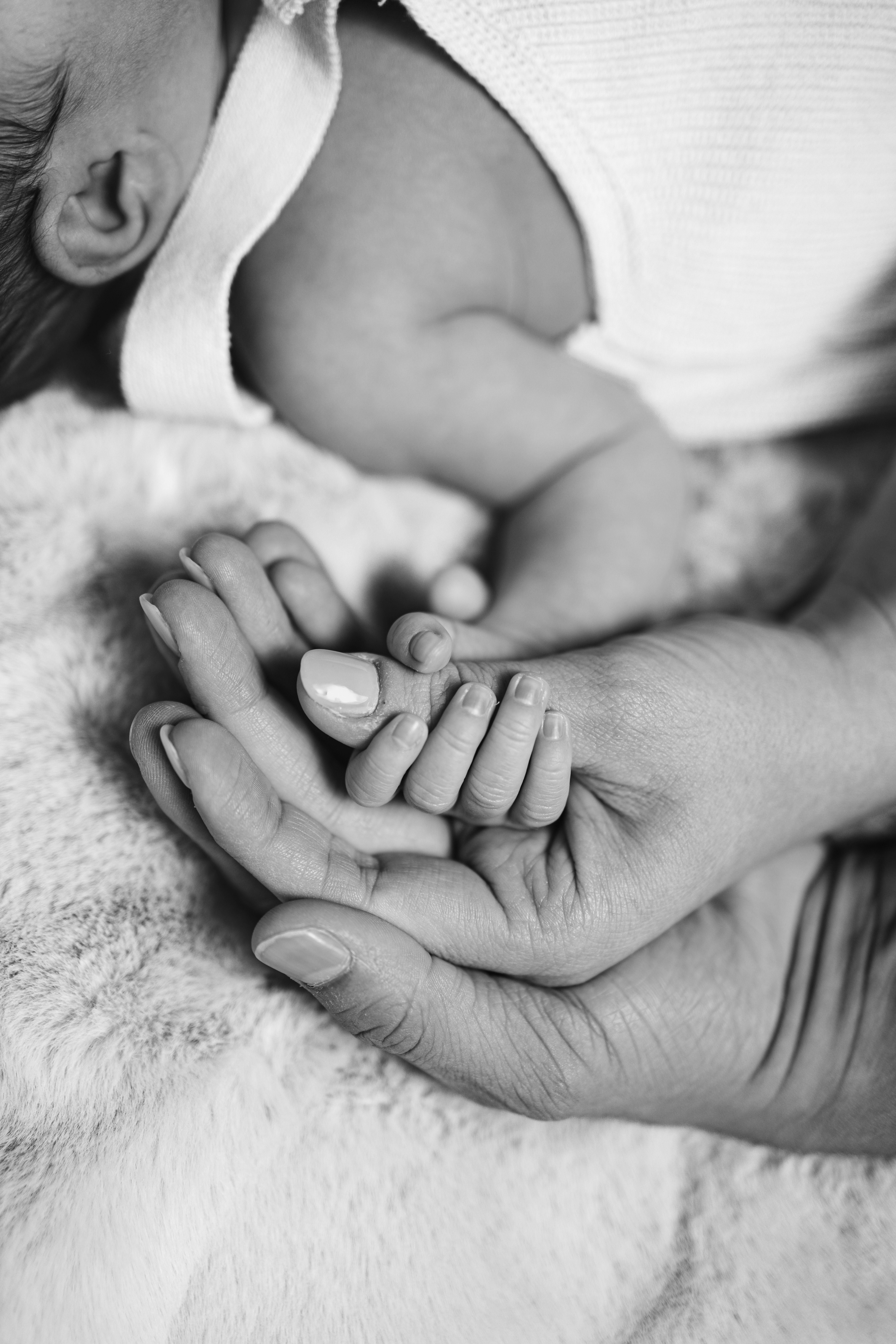 Black and white photo of a newborn baby holding a parent's hand, symbolizing connection and love.