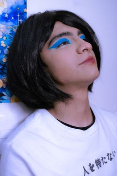 Young adult with striking blue makeup and a black wig in an artistic pose.
