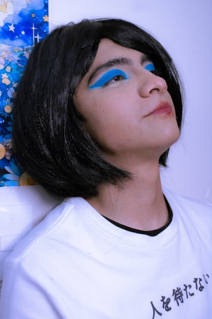 Young adult with striking blue makeup and a black wig in an artistic pose.