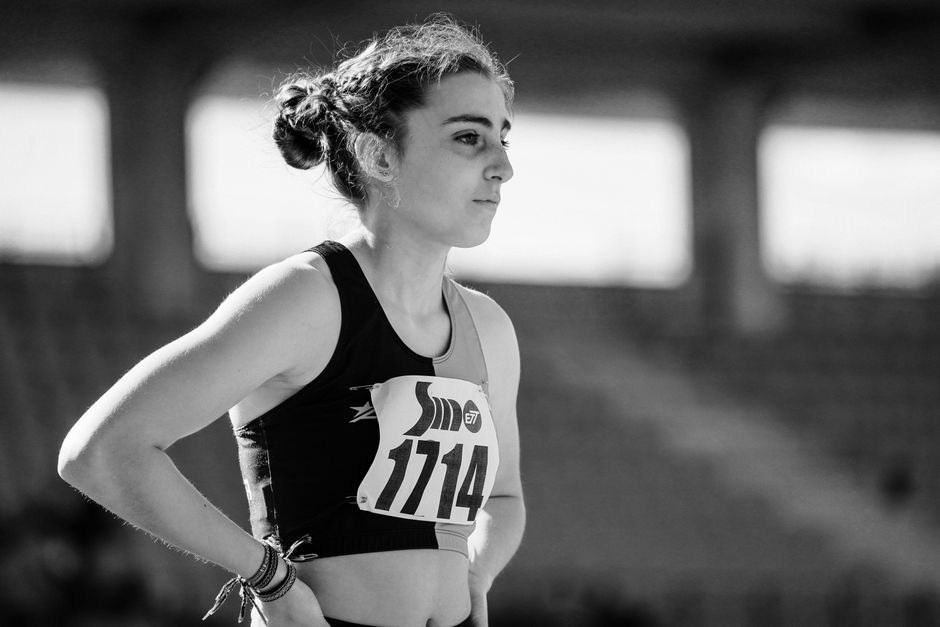 Black and white photo of a female athlete focused before a track competition, wearing bib number 1114.