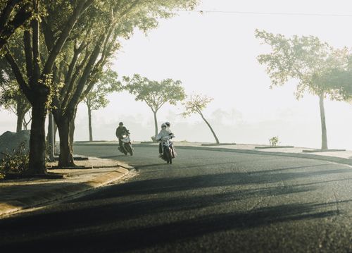 Free Two motorcyclists ride through a misty, tree-lined road in Kon Tum, Vietnam. Stock Photo