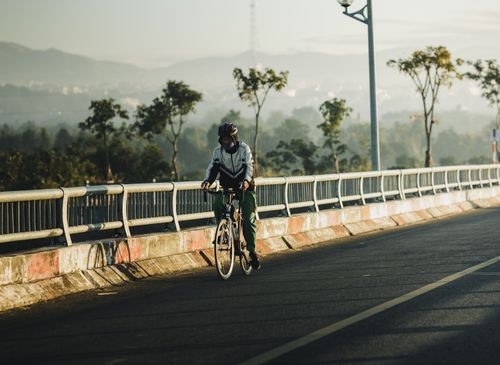 Free A cyclist rides across a scenic bridge in Kon Tum, Vietnam, surrounded by lush greenery and morning light. Stock Photo